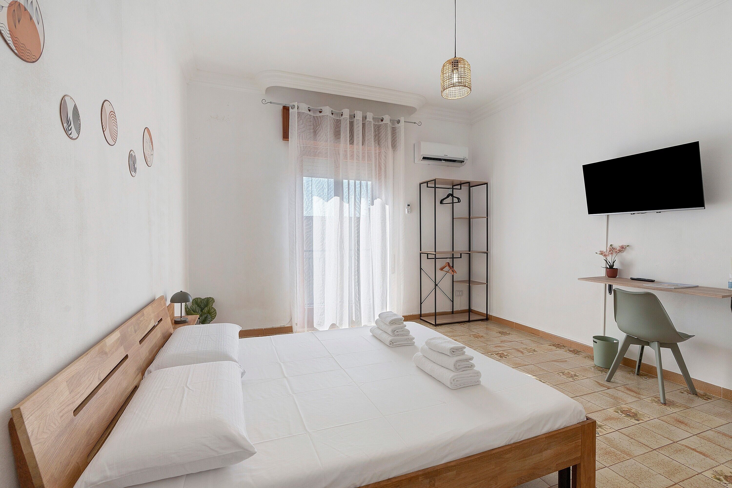 A hotel room with a bed, a desk, a chair, a TV, and a shower area.
