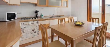 A kitchen with a microwave, stove, sink, and wooden dining table with chairs.