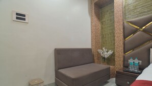 A bedroom with a bed, a nightstand with water bottles, a trash bin, and a wall-mounted air vent. - Shivashish Resort and Marriage Garden (Indore)