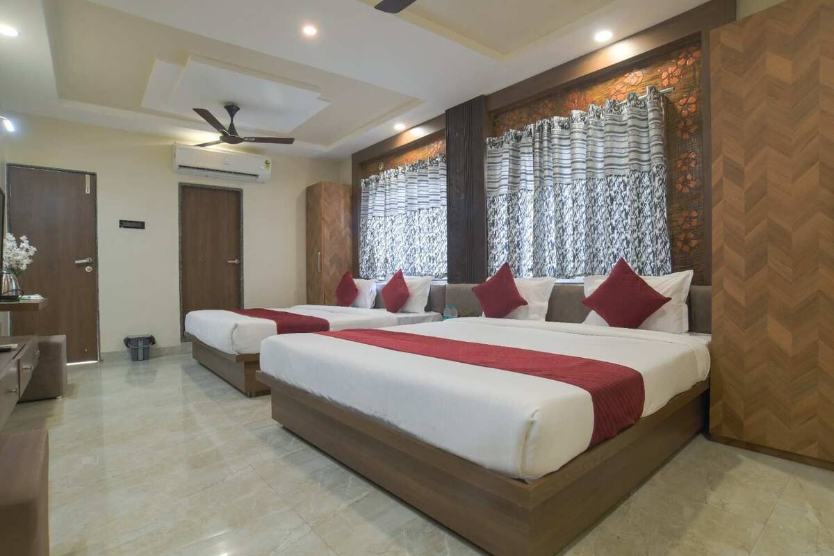 A hotel room with two beds, a desk, a chair, a ceiling fan, and a window with patterned curtains.