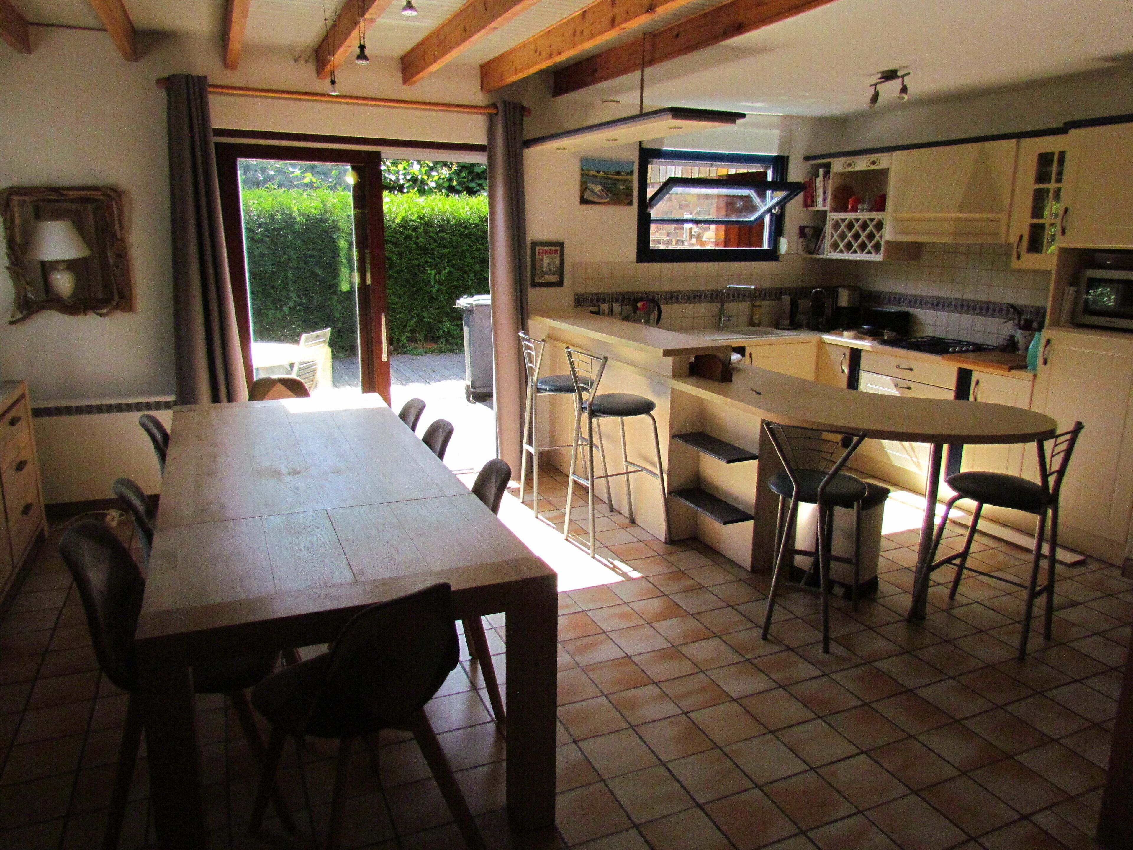 A kitchen with a dining area, a view through a glass door, and a tiled floor.