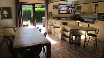 A kitchen with a dining area, a view through a glass door, and a tiled floor.