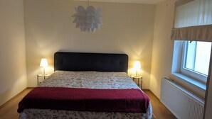Ein Schlafzimmer mit einem Bett, zwei Nachttischlampen, einem Fenster mit Vorhängen und einer Wandleuchte.