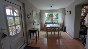 Ein Zimmer mit Esstisch, Stühlen, einer Lampe, einem Fenster mit Vorhängen und einer Tür.