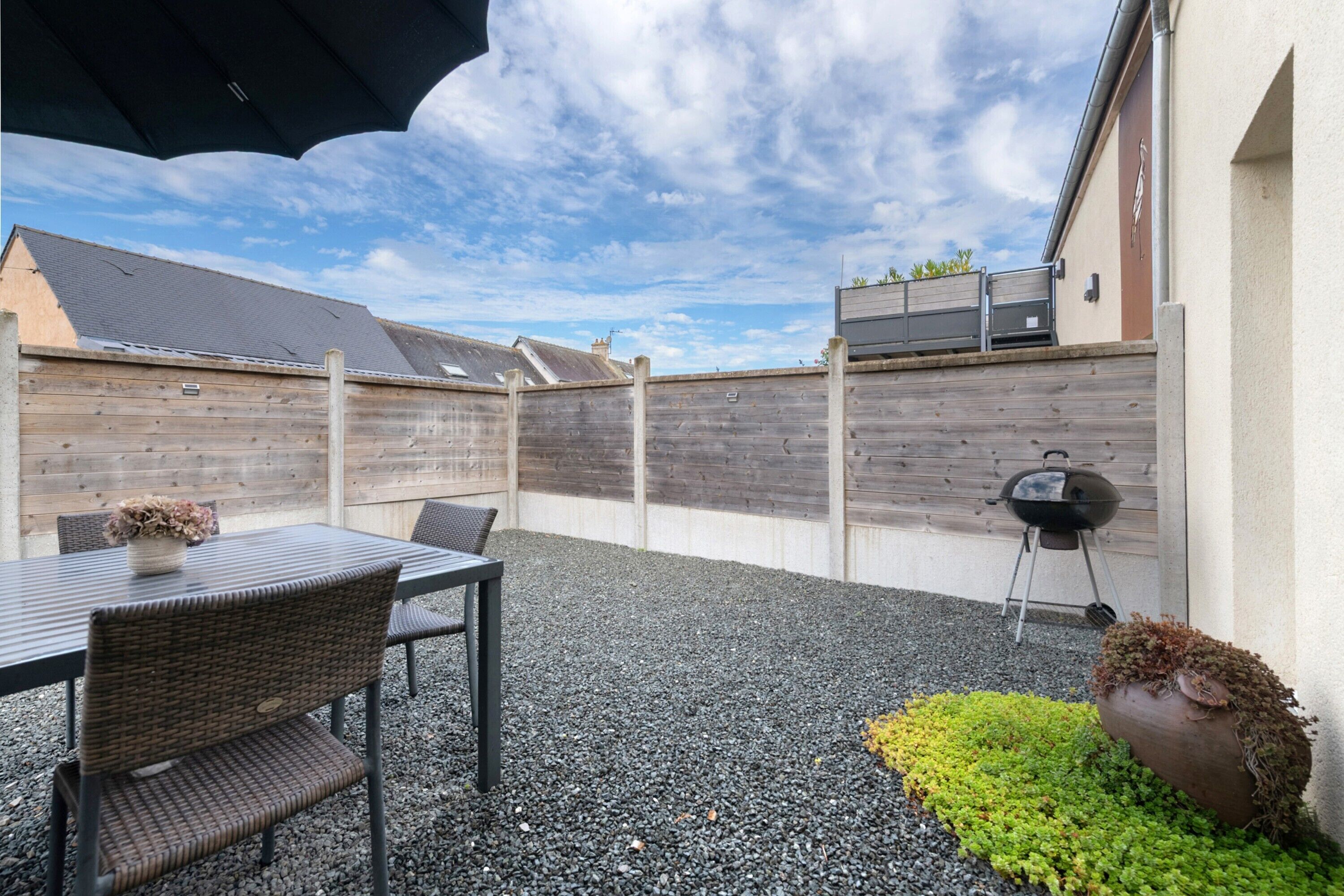 An outdoor patio with a table and chairs, a barbecue grill, and a garden area.