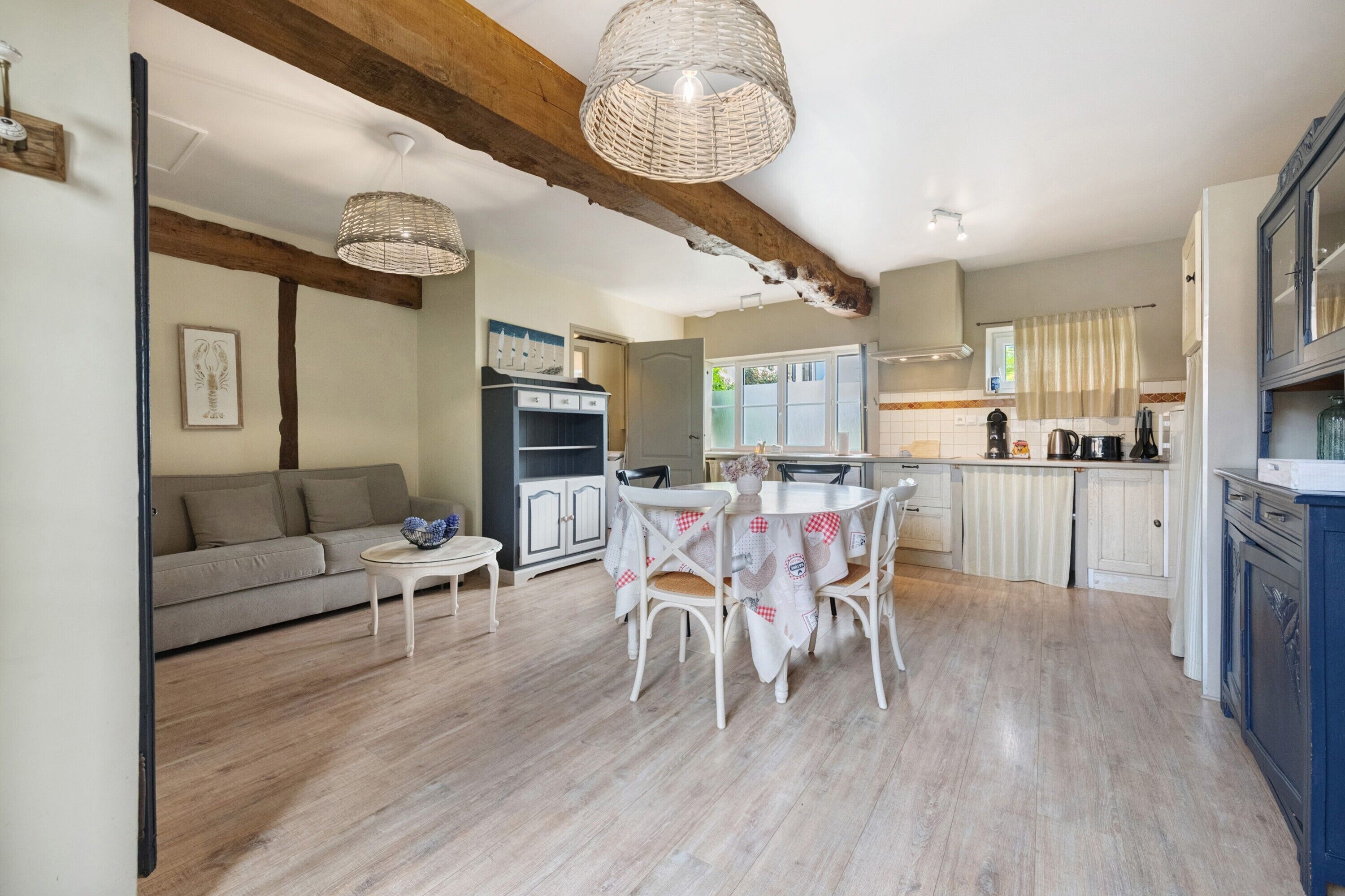 A spacious living area with a sofa, dining table, and chairs, wooden beams on the ceiling, and a kitchen with cabinets and appliances.