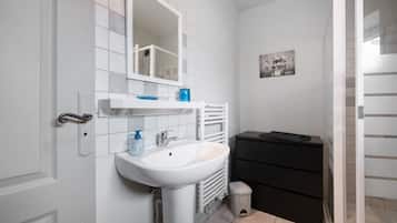 Een badkamer met een witte wasbak, een spiegel, een zwart kastje en een kleine prullenbak.