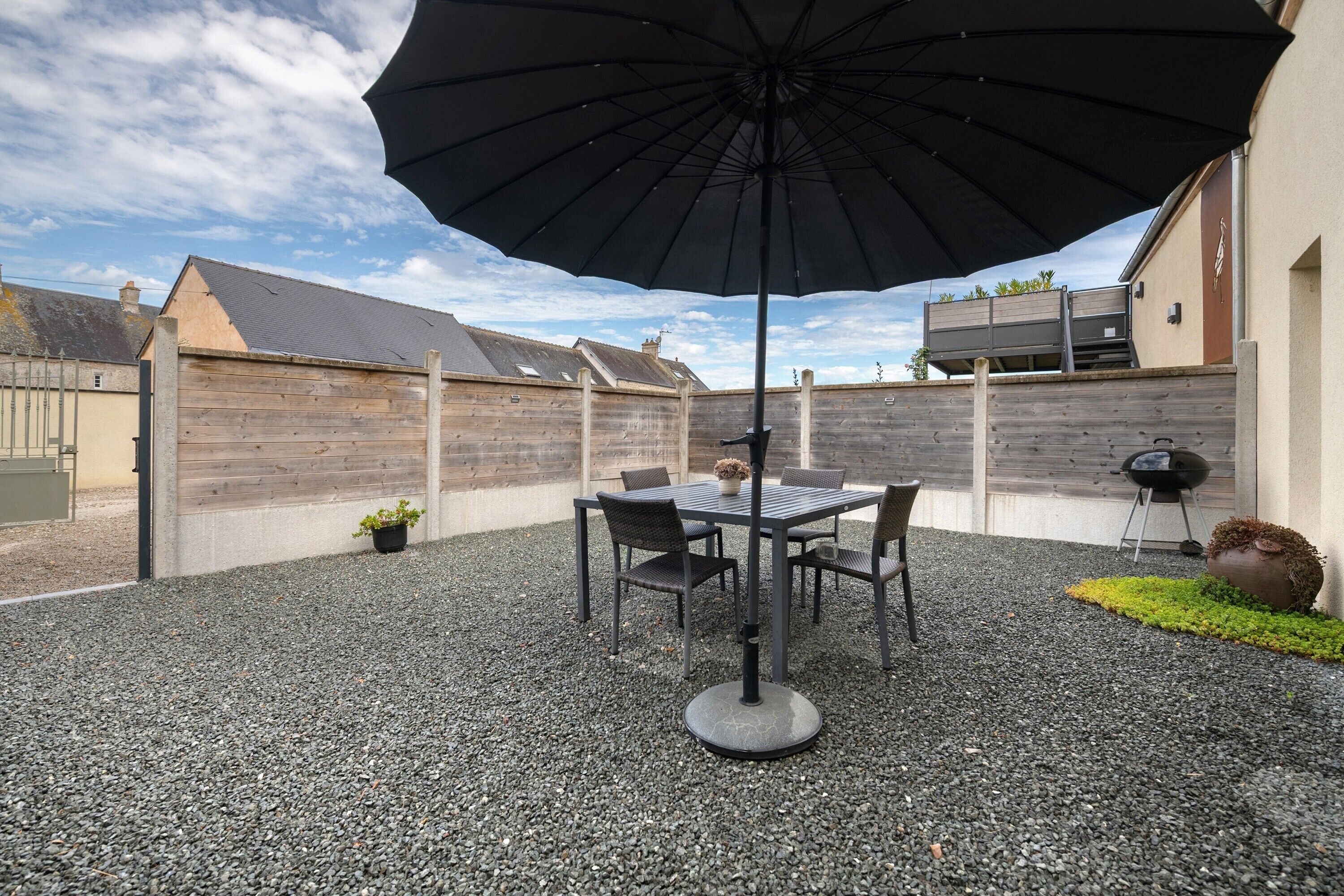 Eine Terrasse im Freien mit Tisch, Stühlen, einem großen Sonnenschirm und einem Grill.