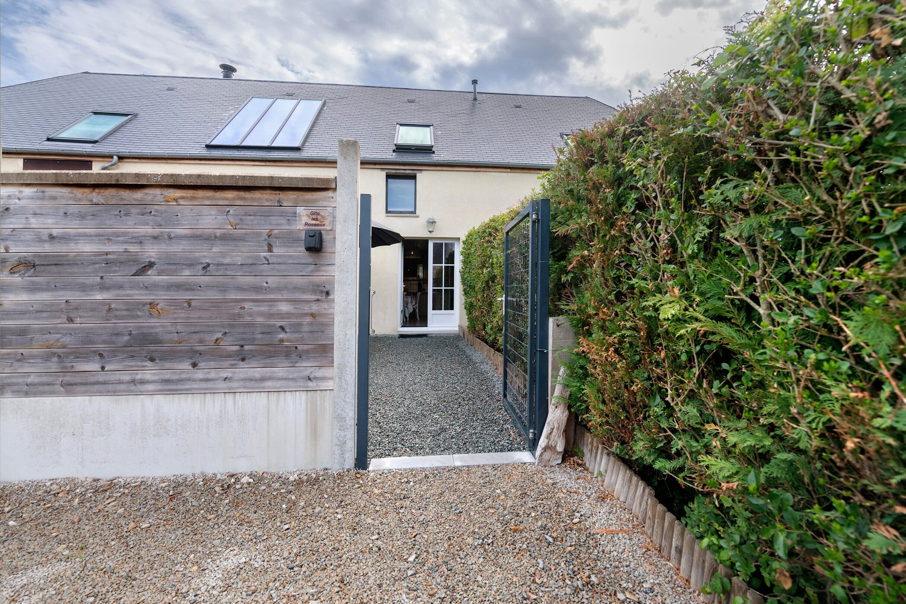 A building with a gravel driveway, wooden fence, and a green gate.