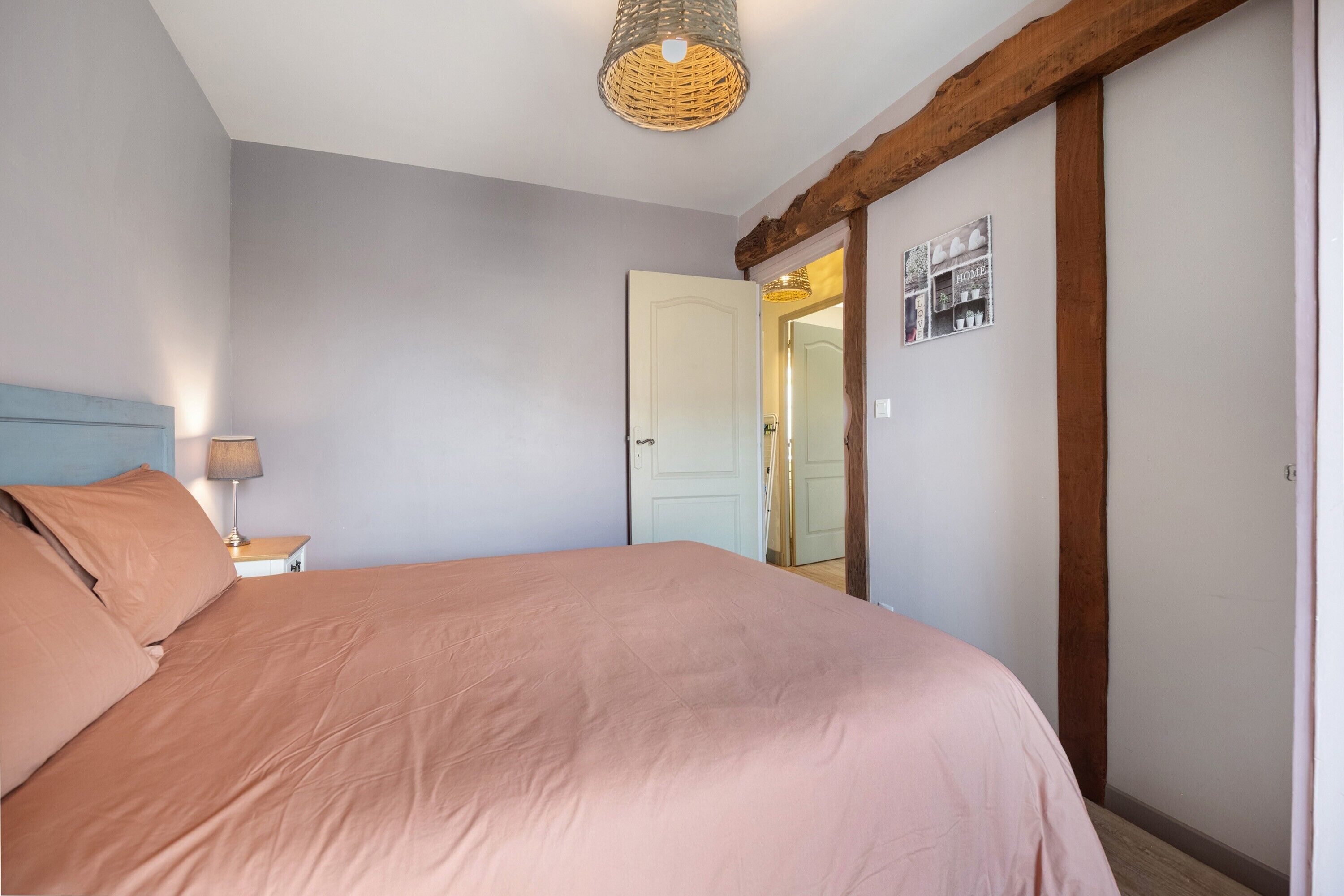 Ein Schlafzimmer mit einem Bett, einem Nachttisch, einer Lampe, einer Tür und einem Wandbild.