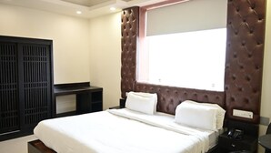 A hotel room with a bed, a desk, a chair, a window, and a wall-mounted TV. - SBM Guest House (Salasar)