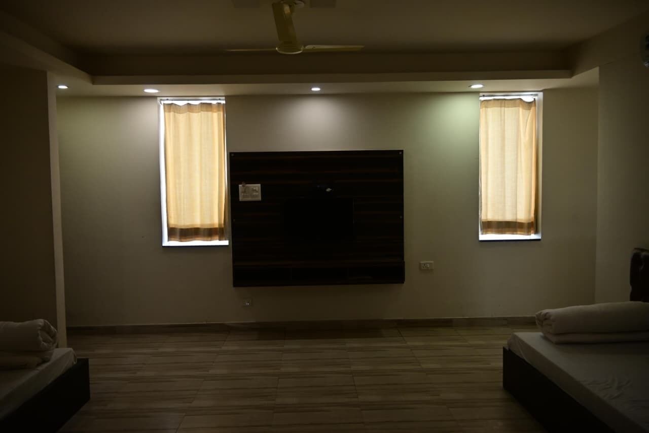 Una habitación con una cama, un televisor de pantalla plana en la pared y dos ventanas con cortinas.