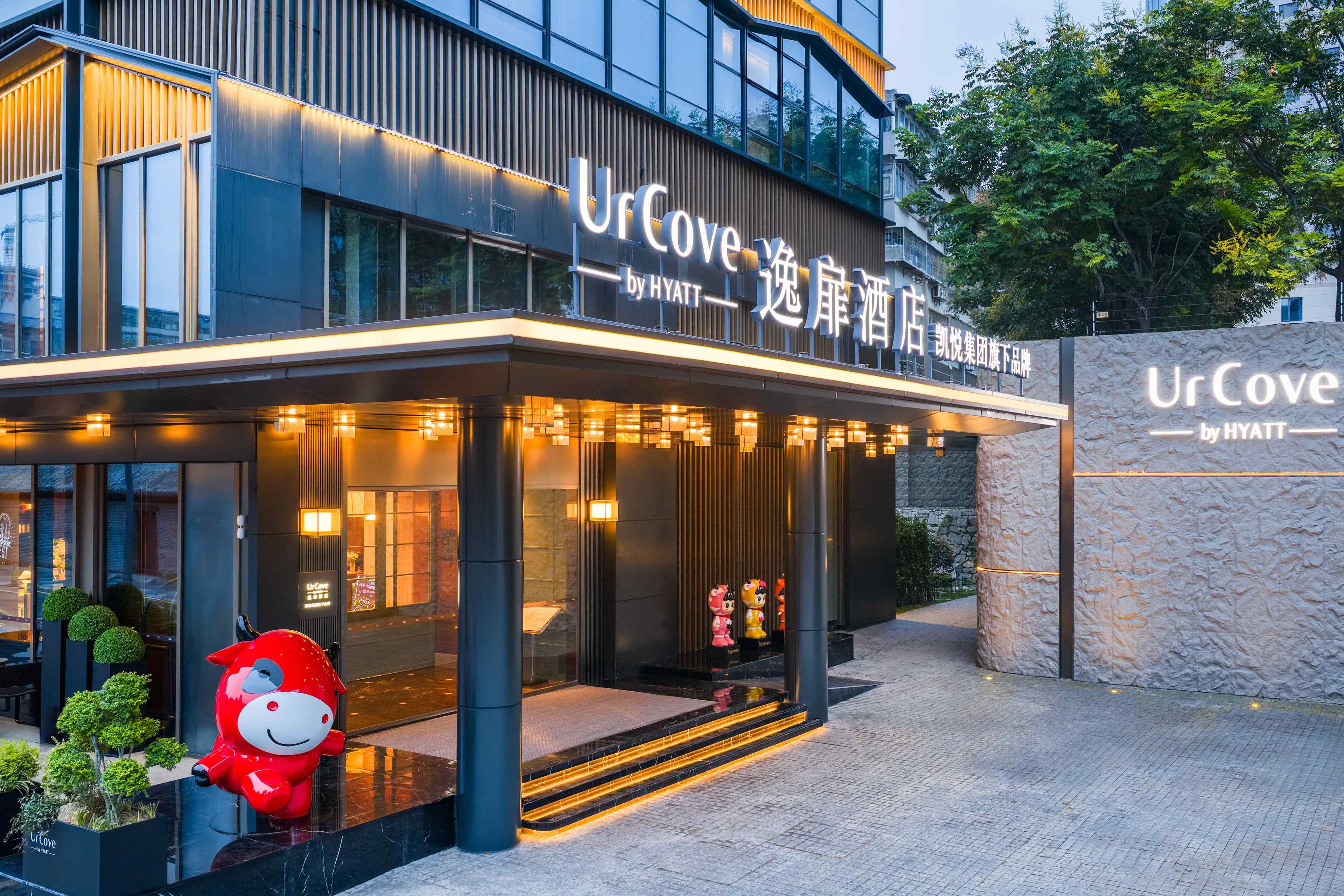 A hotel entrance with a modern design, featuring a large illuminated sign, a welcoming entrance with steps, and a decorative red figure outside.