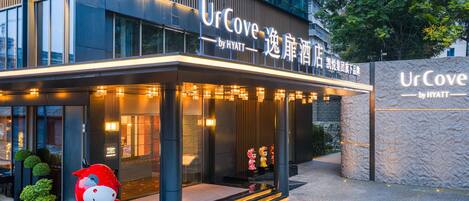 A hotel entrance with a modern design, featuring a large illuminated sign, a welcoming entrance with steps, and a decorative red figure outside.