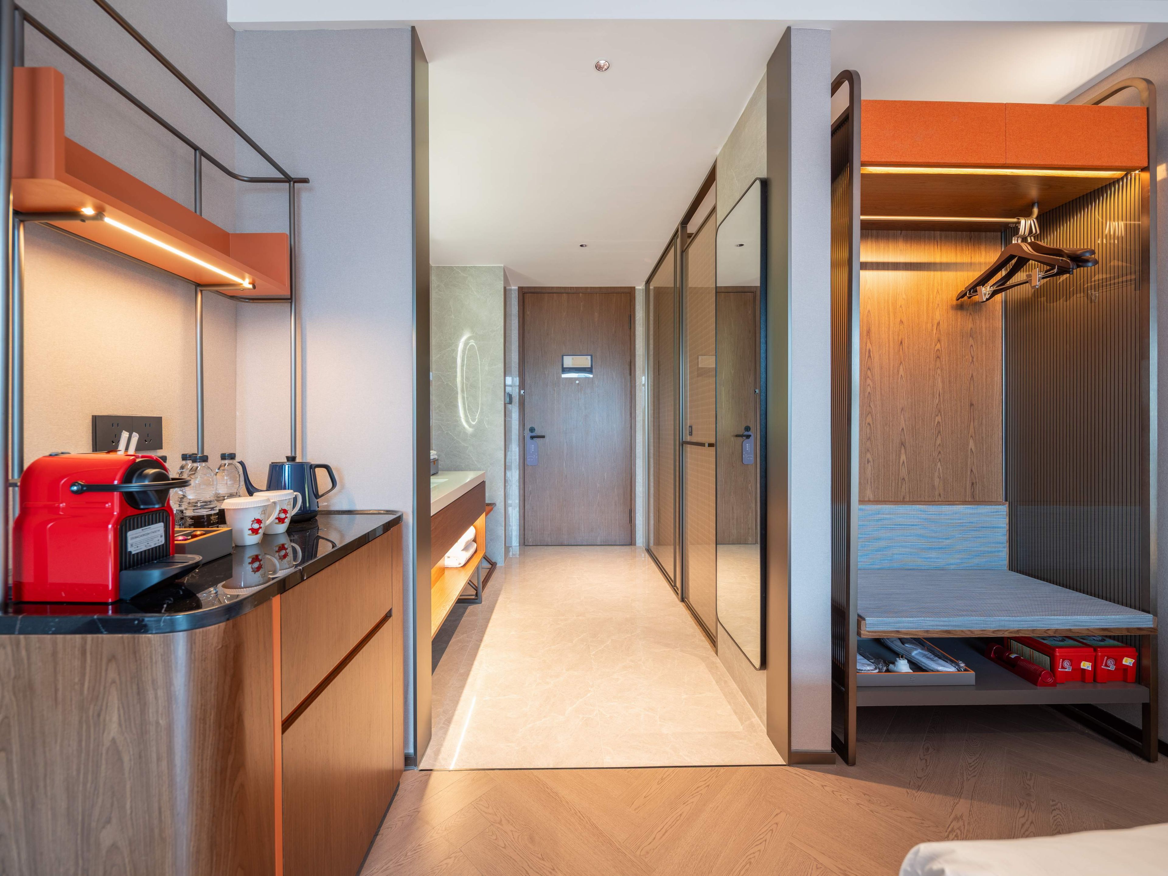 A modern hotel room with a kitchenette, a bed with storage, and a walk-in closet.