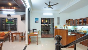 A spacious living area with a dining table, chairs, a sofa, a kitchen with wooden cabinets, a ceiling fan, and a staircase. - Old Lane Hoi An Homestay (Hoi An)