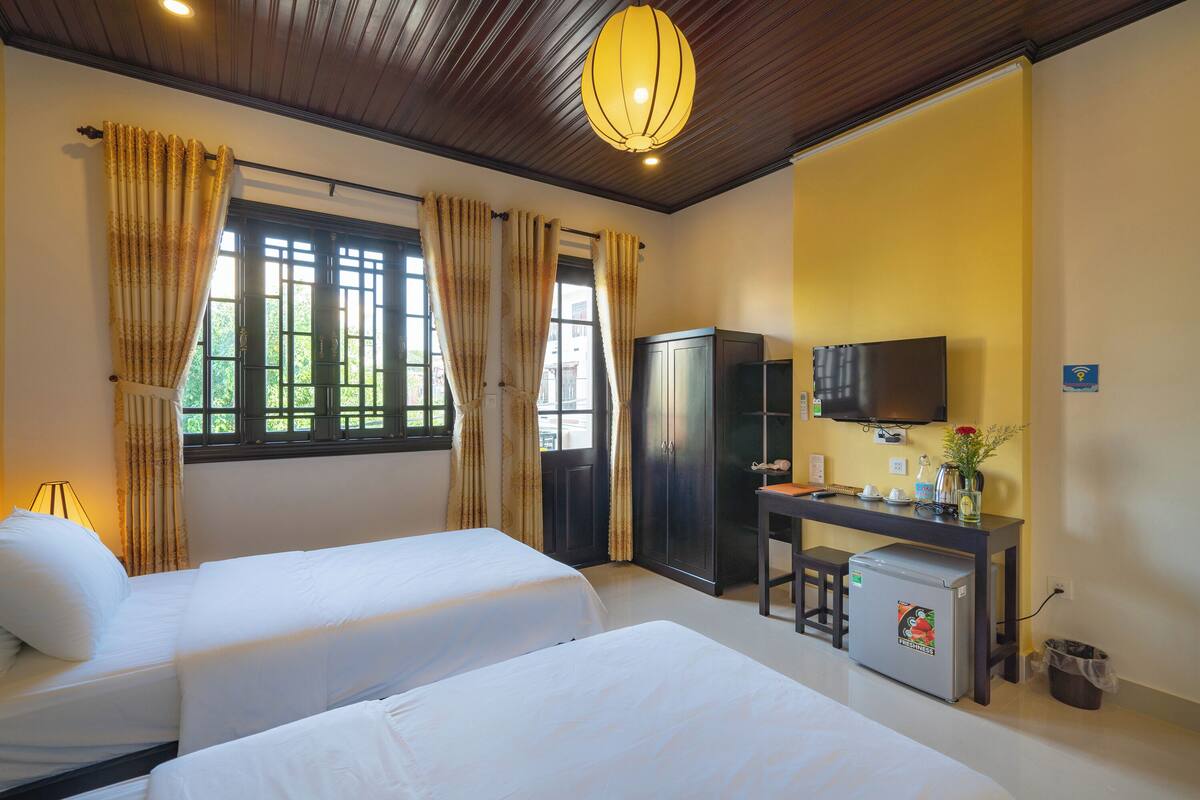 A hotel room with two beds, a desk with a television, a refrigerator, and a window with curtains.