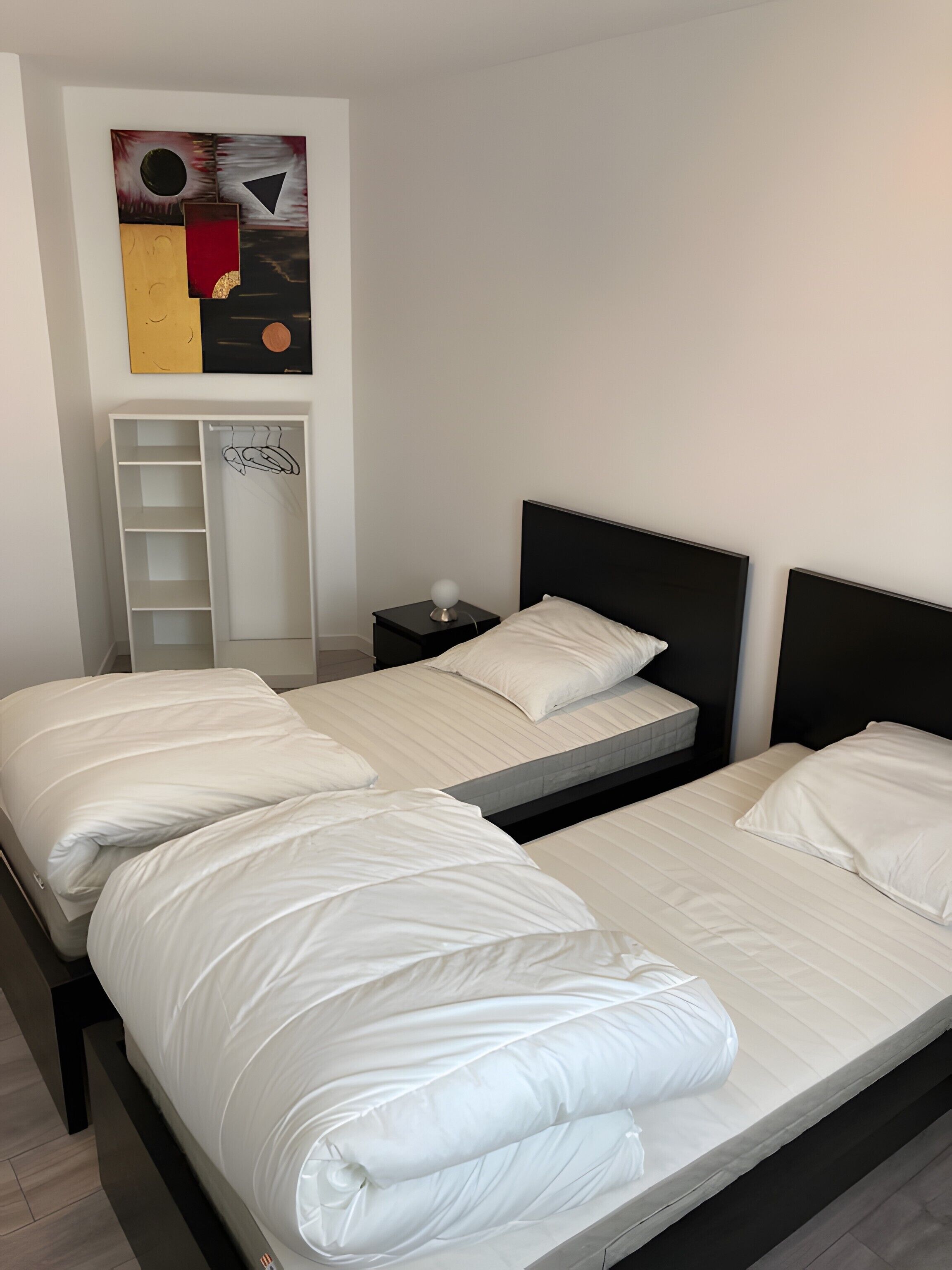 Ein Schlafzimmer mit zwei Betten, einem Nachttisch, einem Wandbild und einer Ablage.