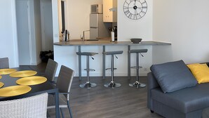 Una cocina moderna con un reloj, un comedor con mesa y sillas, y un sofá gris.
