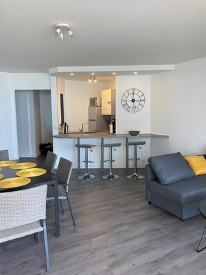 Eine moderne Küche mit einer Uhr, ein Essbereich mit Tisch und Stühlen sowie ein graues Sofa.