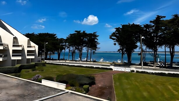 Un edificio moderno con vista despejada al mar, rodeado de árboles y un césped cuidado.
