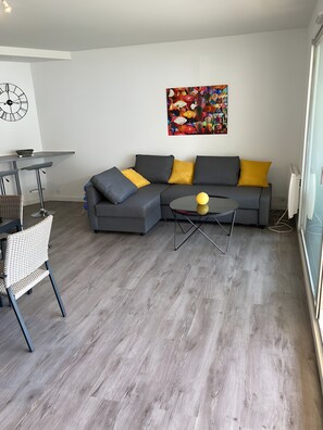 A modern living room with a grey sectional sofa, a small round coffee table, and a colorful abstract painting on the wall. - Charming Seafront Apartment in Le Croisic (Le Croisic)