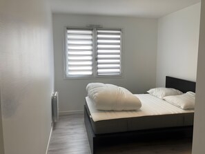 Ein Schlafzimmer mit einem Bett, einem Fenster mit Jalousien, einem Heizkörper und einem Holzboden.