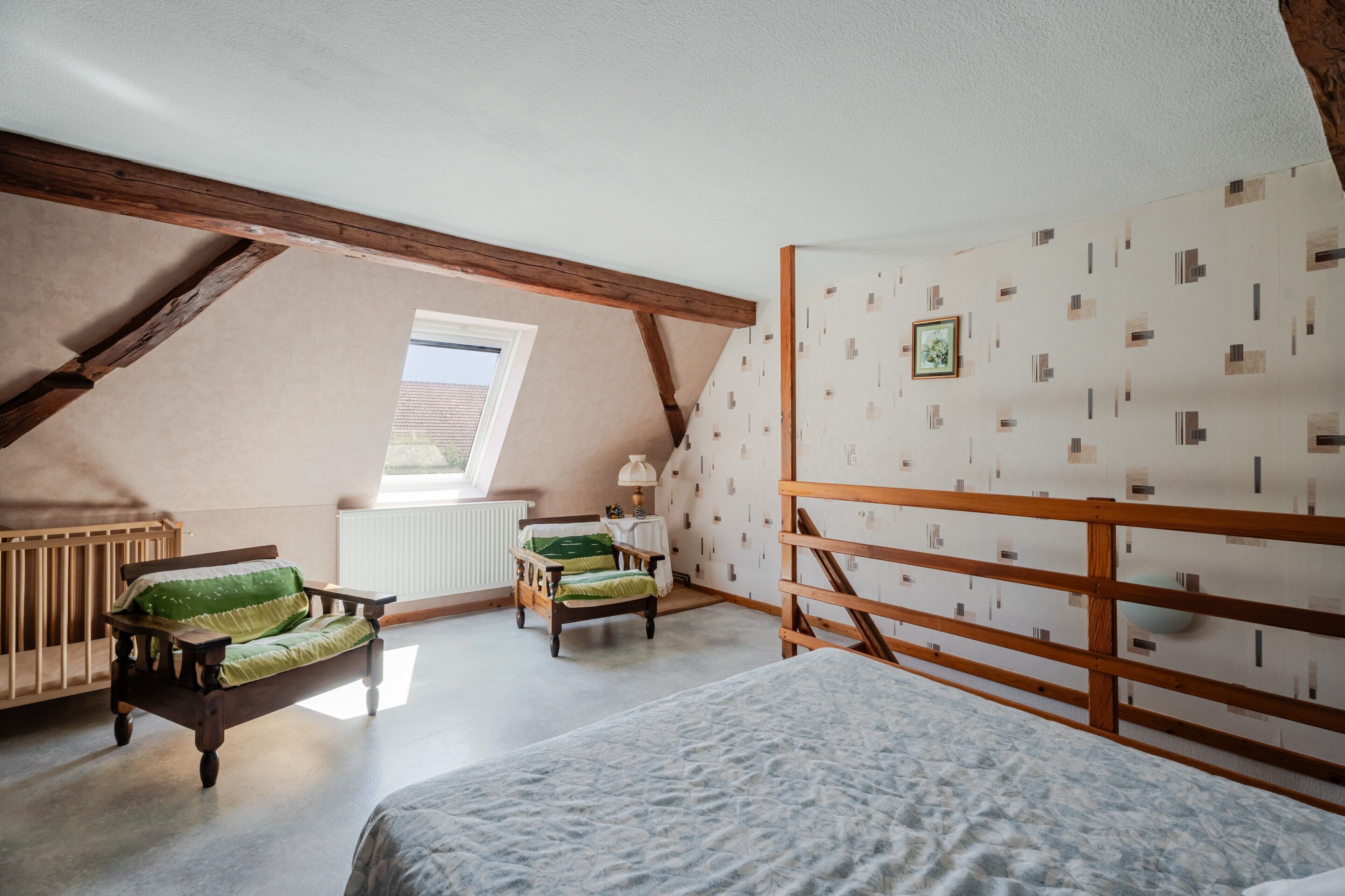 A room with a sloped ceiling, a crib, a bed, a wooden bench, and a small table with a lamp.