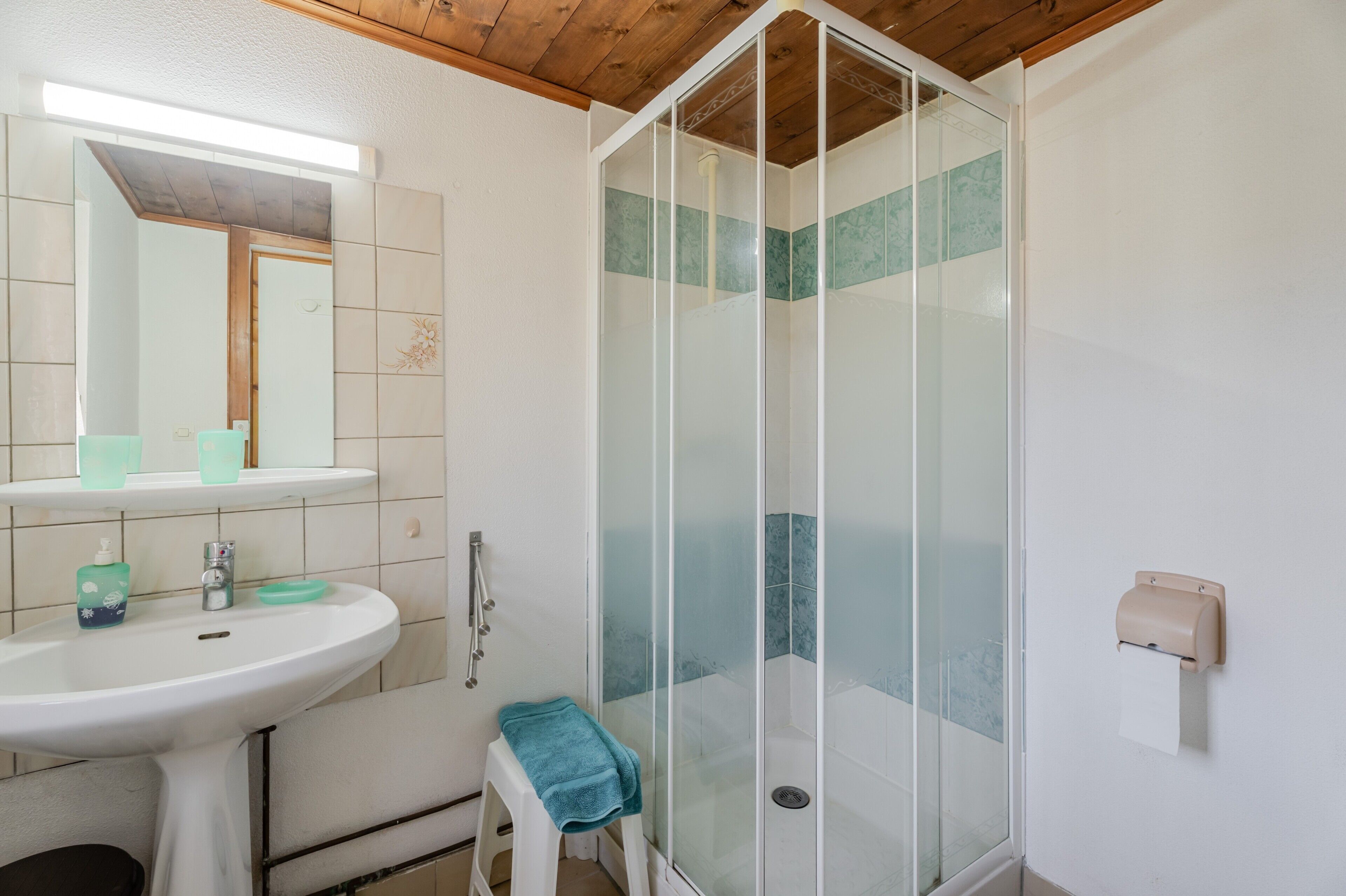 Ein Badezimmer mit einer gläsernen Duschkabine, einem Waschbecken mit Spiegel und einem Handtuchhalter.