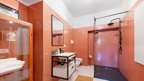 Un baño con cabina de ducha de vidrio, un lavamanos blanco y un armario de vidrio con toallas.