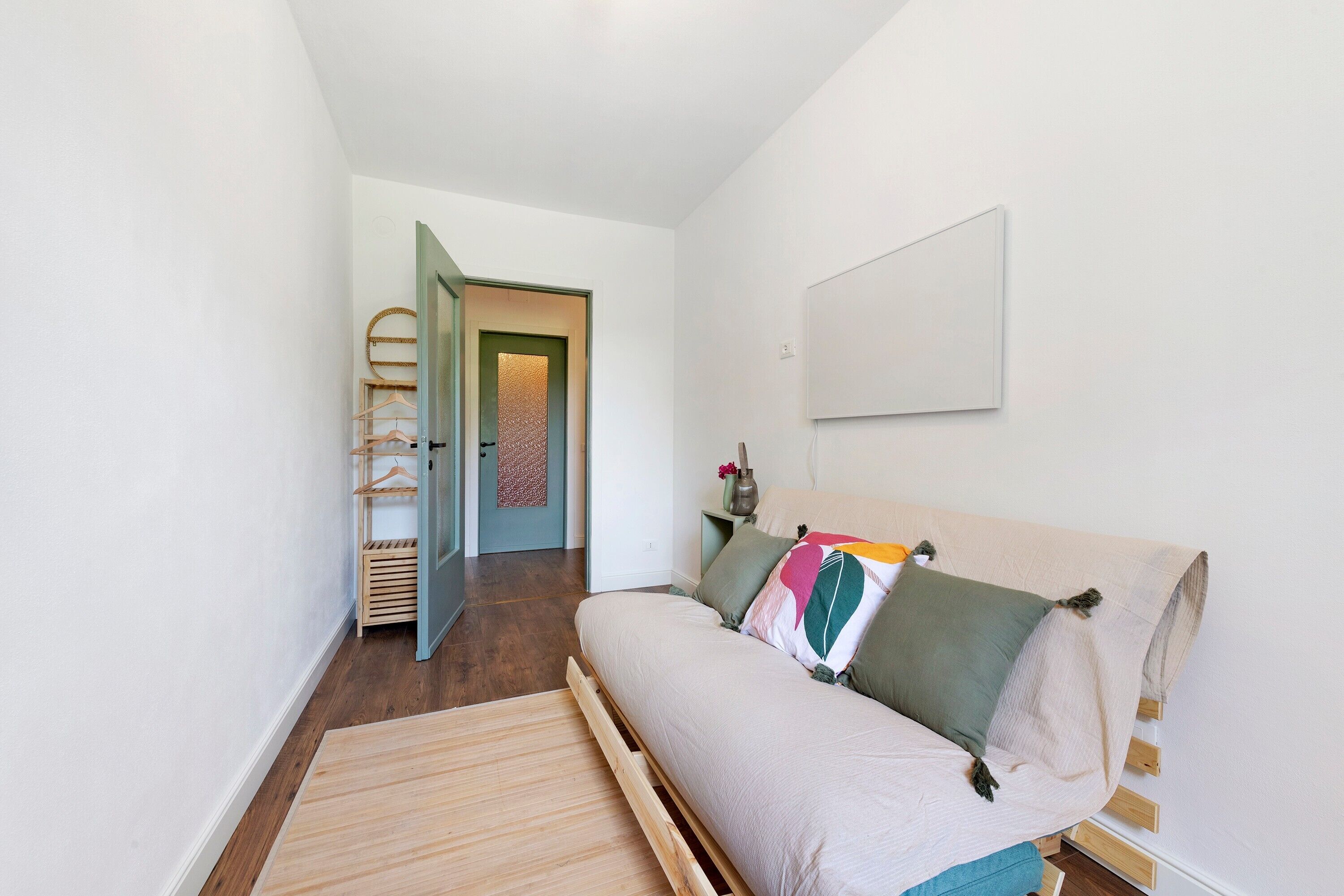 Ein Schlafzimmer mit einem Bett, Holzboden, einer Tür und einem an der Wand befestigten Regal.