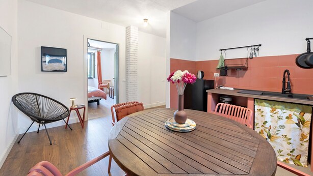 Un comedor con una mesa redonda de madera, una silla negra y una silla rosa. Hay un jarrón con flores sobre la mesa.