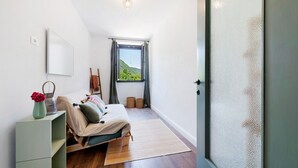 Un dormitorio con cama, un escritorio pequeño, una ventana con cortinas y vista a follaje exterior.