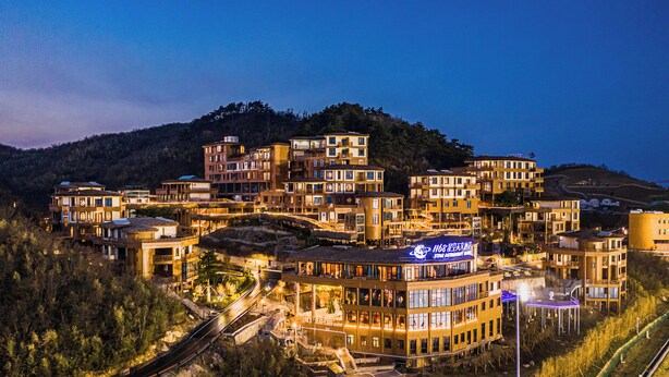 A multi-story hotel with a rooftop bar, surrounded by hills and a train track. - 1168 Starry Sky Astronomy Hotel (Huzhou)