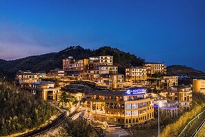 A multi-story hotel with a rooftop bar, surrounded by hills and a train track. - 1168 Starry Sky Astronomy Hotel (Huzhou)