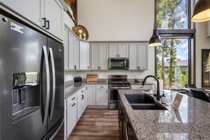 A modern kitchen with stainless steel appliances, granite countertops, and a large window offering a view of trees. - Twilight Pines Cabin (Lead)
