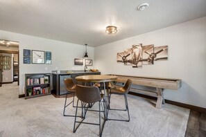 A modern kitchen with a dining area, featuring a round table, bar stools, a bookshelf, and a bench.