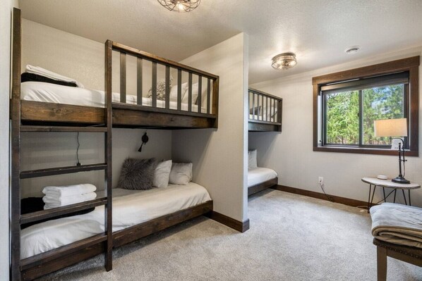 A room with bunk beds, a small table with a lamp, and a window with a view of greenery.