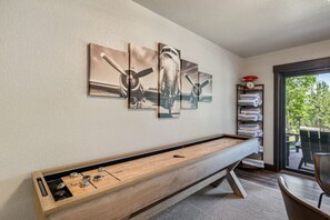 A pool table with a wooden finish and metal accents, a wall with abstract art, a bookshelf with towels, and a view through a glass door.