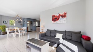 Un salon moderne avec un canapé gris, une table basse et un coin repas comprenant une table et des chaises blanches.
