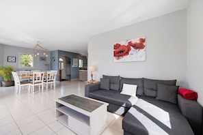 A modern living room with a grey sofa, a coffee table, and a dining area with a white table and chairs.
