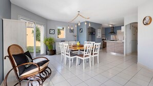 Un coin repas avec une table et des chaises, un fauteuil à bascule, un lustre et, au fond, une cuisine.