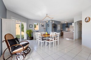 A dining area with a table and chairs, a rocking chair, a chandelier, and a kitchen in the background.