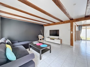 En moderne stue med sofa, sofabord med farvede skiver, fjernsyn og træloft.