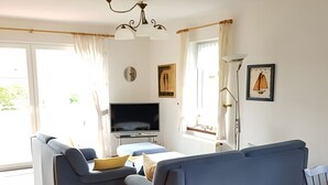 A modern living room with a sofa, TV, and a dining area. - Holiday Home 'House Kiki in Dornumersiel' with Private Terrace, Private Garden and Wi-Fi (Dornum)