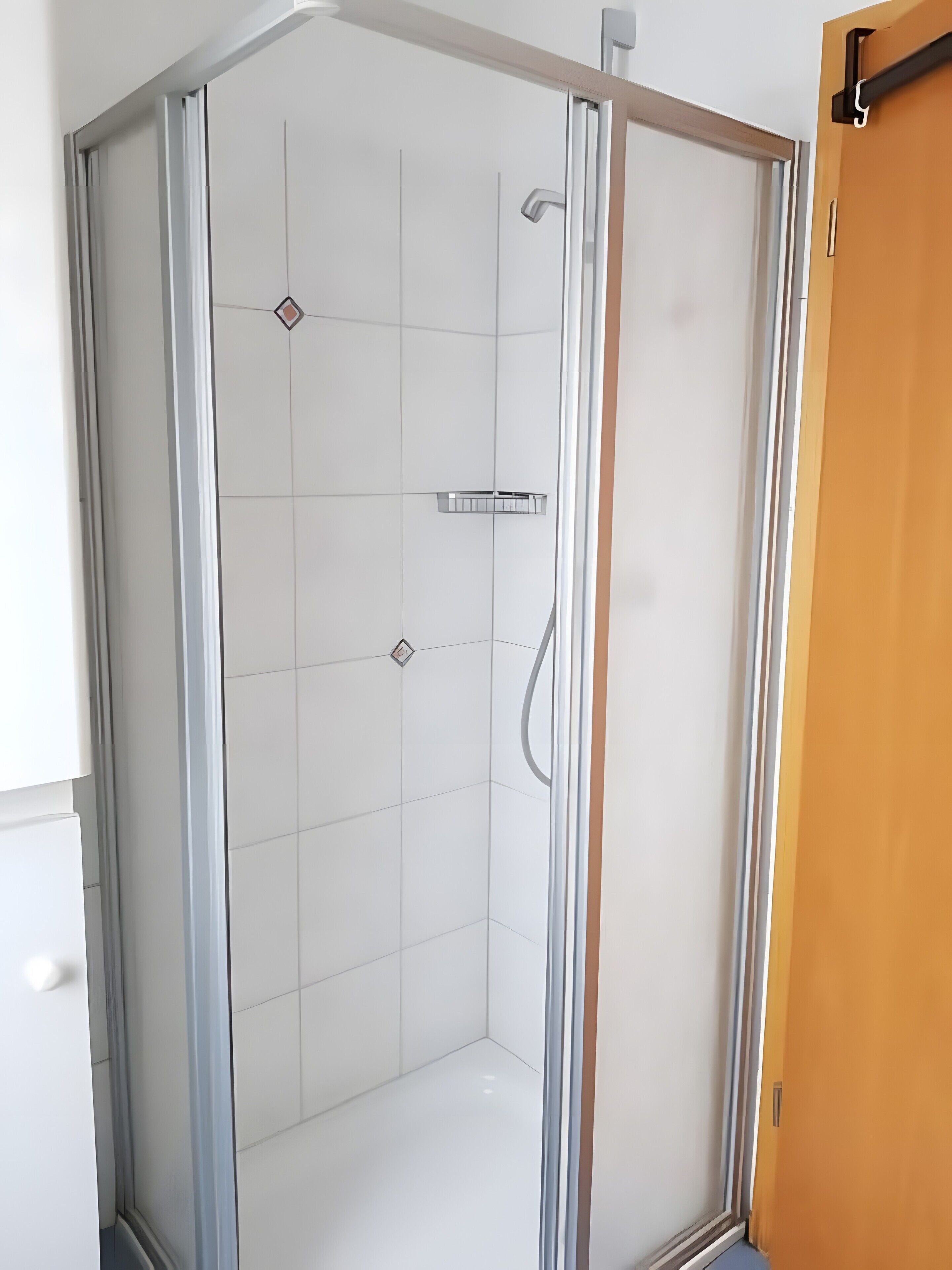 Une douche d’angle avec des carreaux blancs, une pomme de douche chromée et une porte en verre.