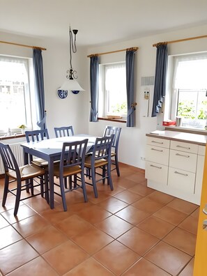 Ein Essbereich mit Tisch und Stühlen, eine Küche mit Schränken und ein Fenster mit Vorhängen.