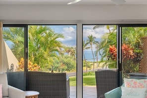 Ein Zimmer mit Blick auf Palmen und Meer, mit Korbmöbeln und einem Kissen mit der Aufschrift 'Aloha'.