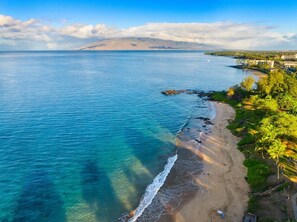 Uma praia costeira com águas claras, areal arenoso e montanhas ao longe.