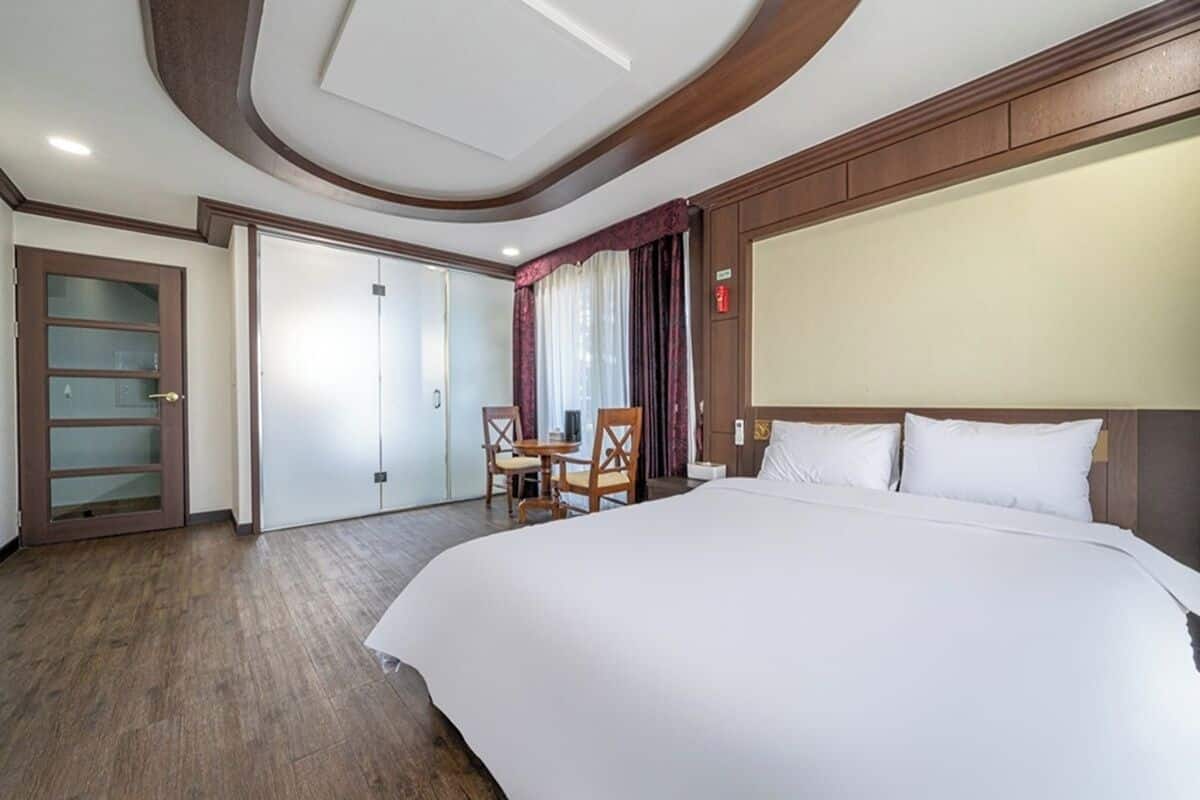 Een hotelkamer met een groot bed, een bureau met twee stoelen, een kast en een deur naar een andere kamer.